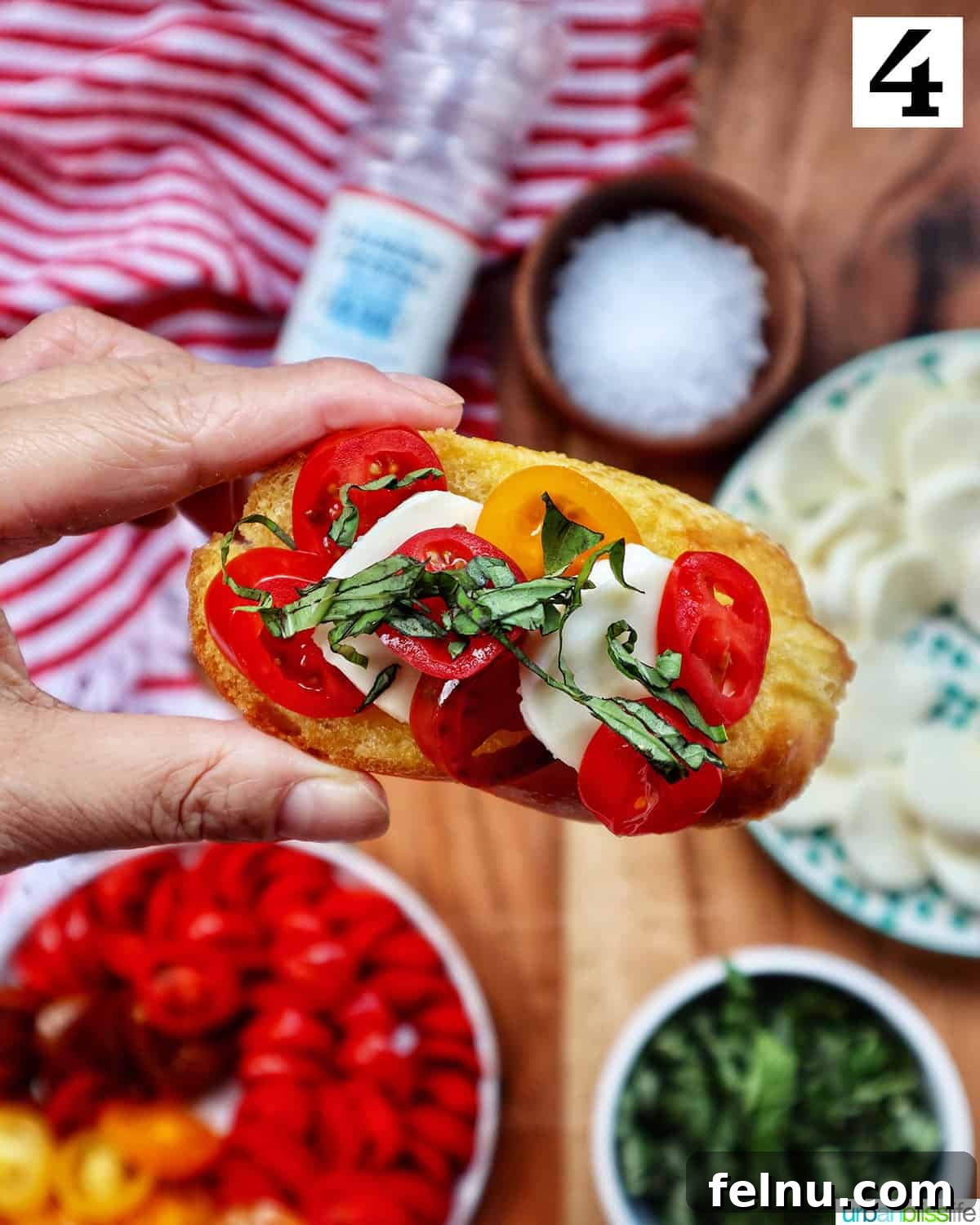 A close-up of a hand arranging a Caprese Crostini with tomato, mozzarella, and basil on a rustic wooden board, ready for serving.