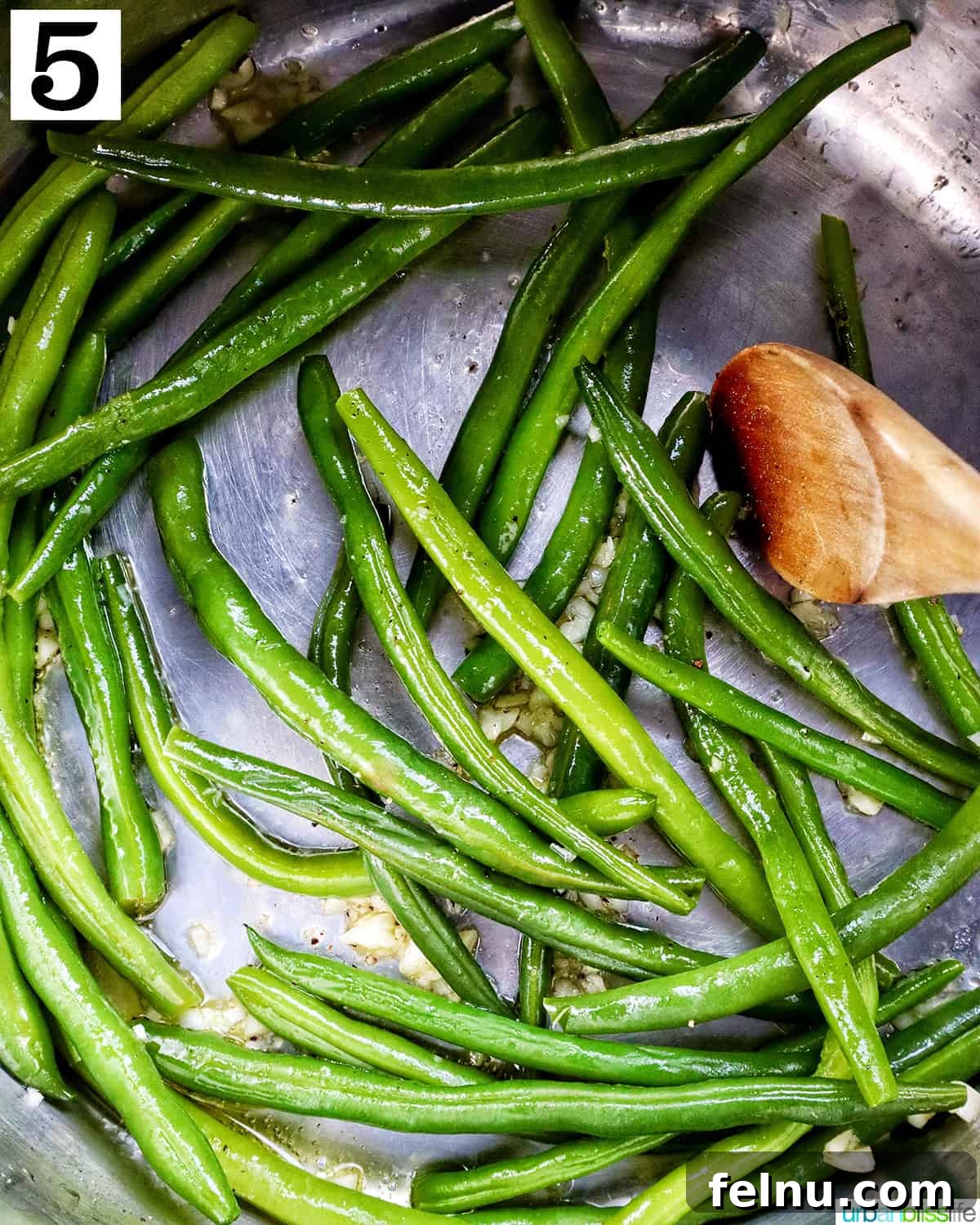 Stirring green beans with a wooden spoon in the Instant Pot after sauteing with garlic.