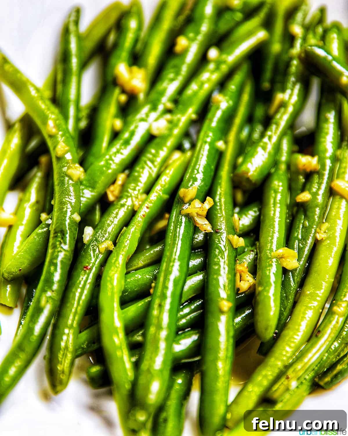 Close-up shot of garlic green beans in a white bowl, highlighting their appealing texture and aroma.