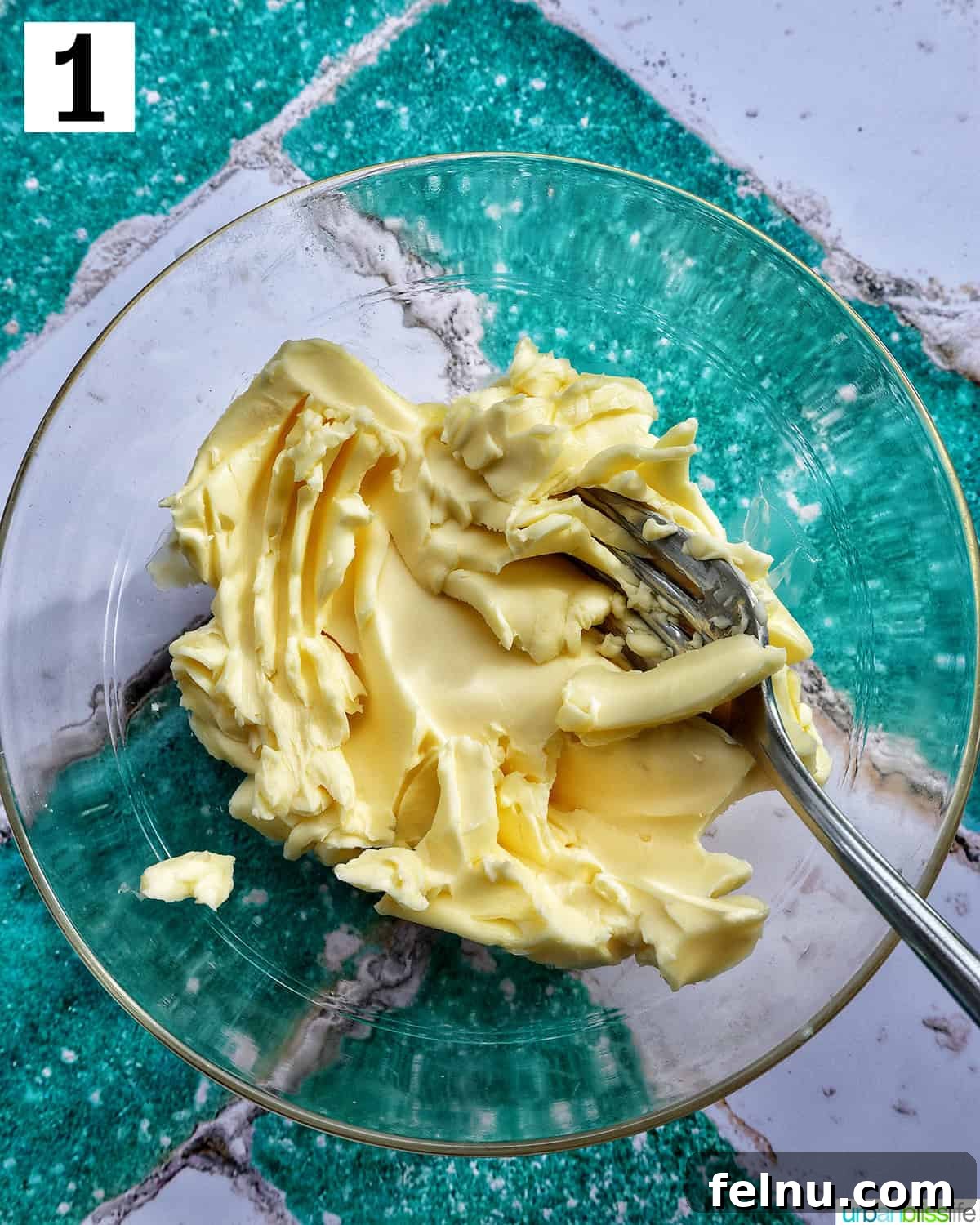 Softened butter mashed with a fork in a clear bowl.