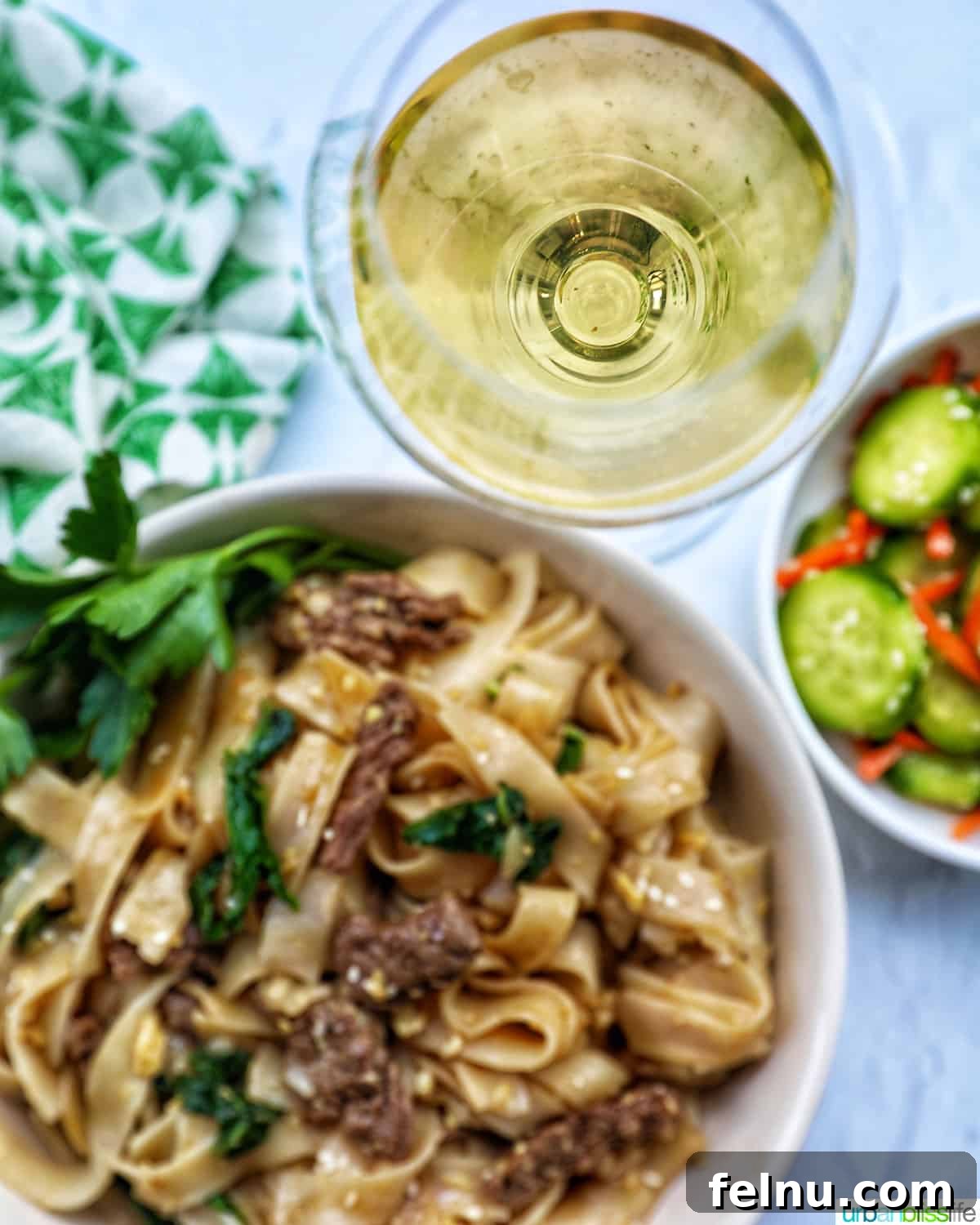 Pad See Ew Versus Pad Thai Your Ultimate Noodle Showdown 6 A bowl of beef Pad See Ew noodles with bok choy, a glass of white wine, and a side of cucumber salad.