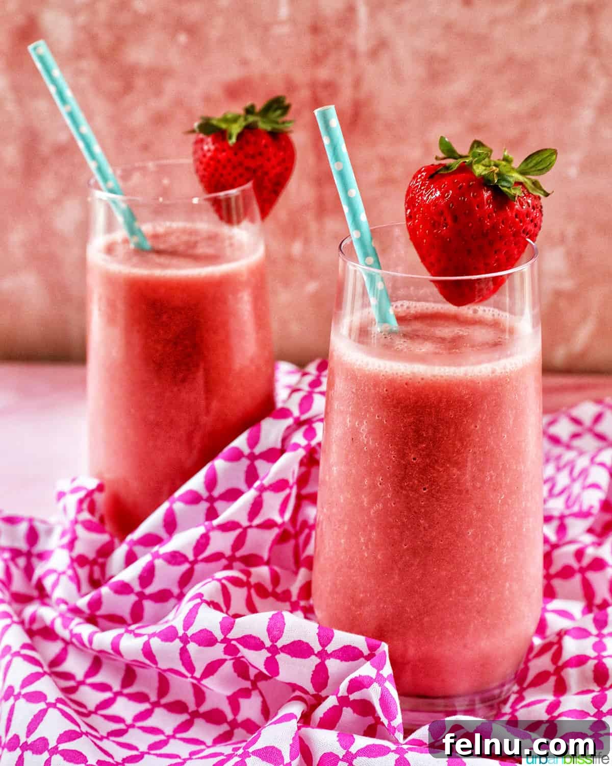 Strawberry Watermelon Refresher 2 Two glasses filled with strawberry watermelon smoothie, garnished with sliced strawberries and blue straws on a pink and white napkin.