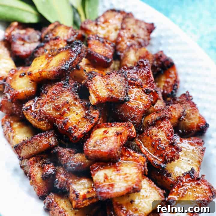 pile of air fryer pork belly bites on a white serving platter with bay leaves on a blue background.