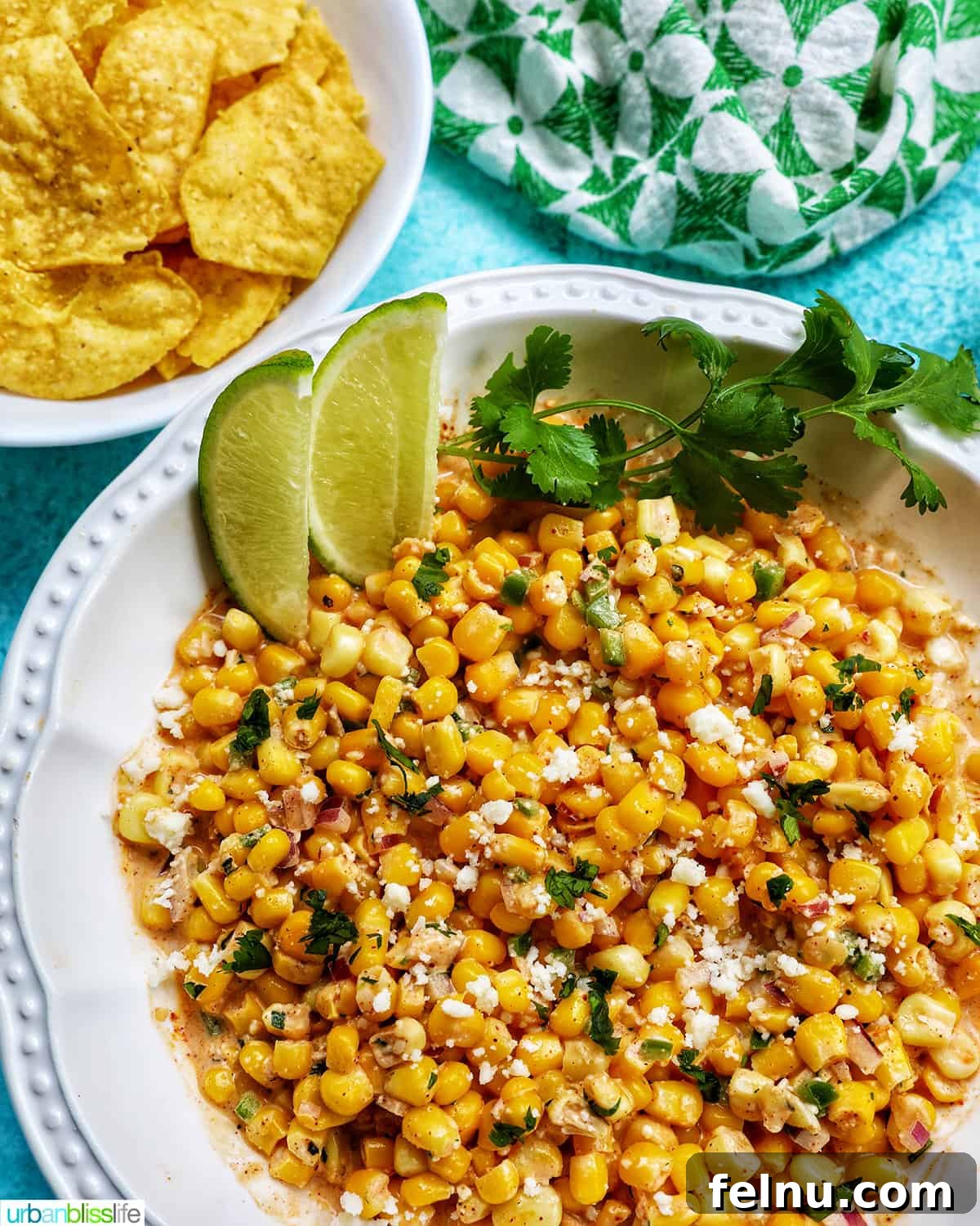 Mexican Street Corn Fiesta Dip 8 Large bowl of Elote Dip (Mexican corn dip) surrounded by a bowl of tortilla chips, fresh lime wedges, and cilantro for garnishing.