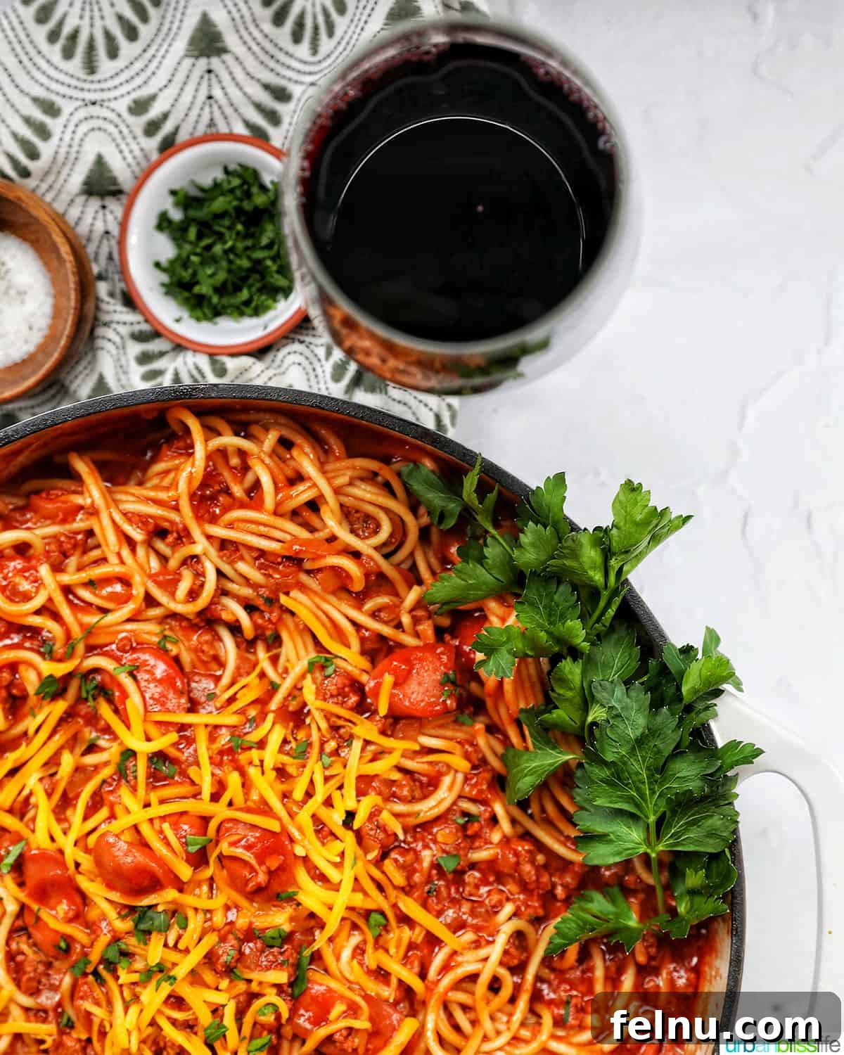 Uncorking Pasta Perfection 4 Filipino-style spaghetti in a saucepan with glass of red wine and side of salt, pepper, parsley, shredded cheese.