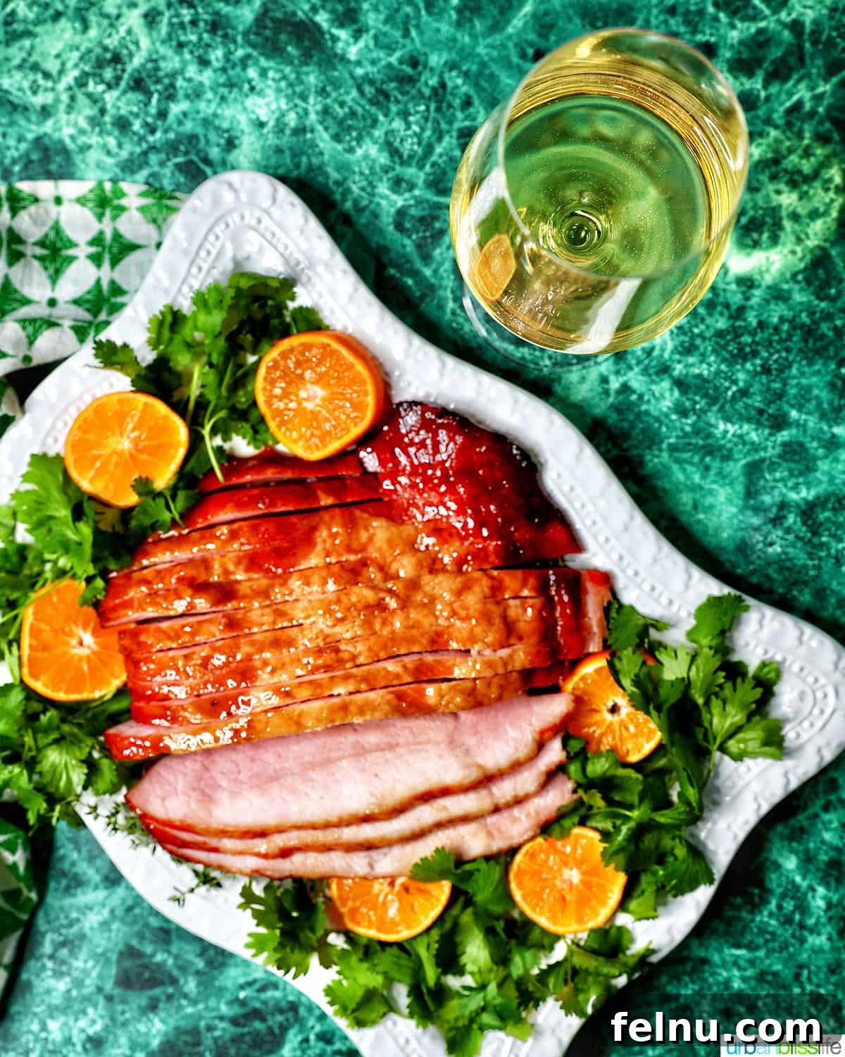 Elevate Your Ham with the Perfect Wine 4 Glass of white wine behind a platter of honey glazed ham with garnishes.