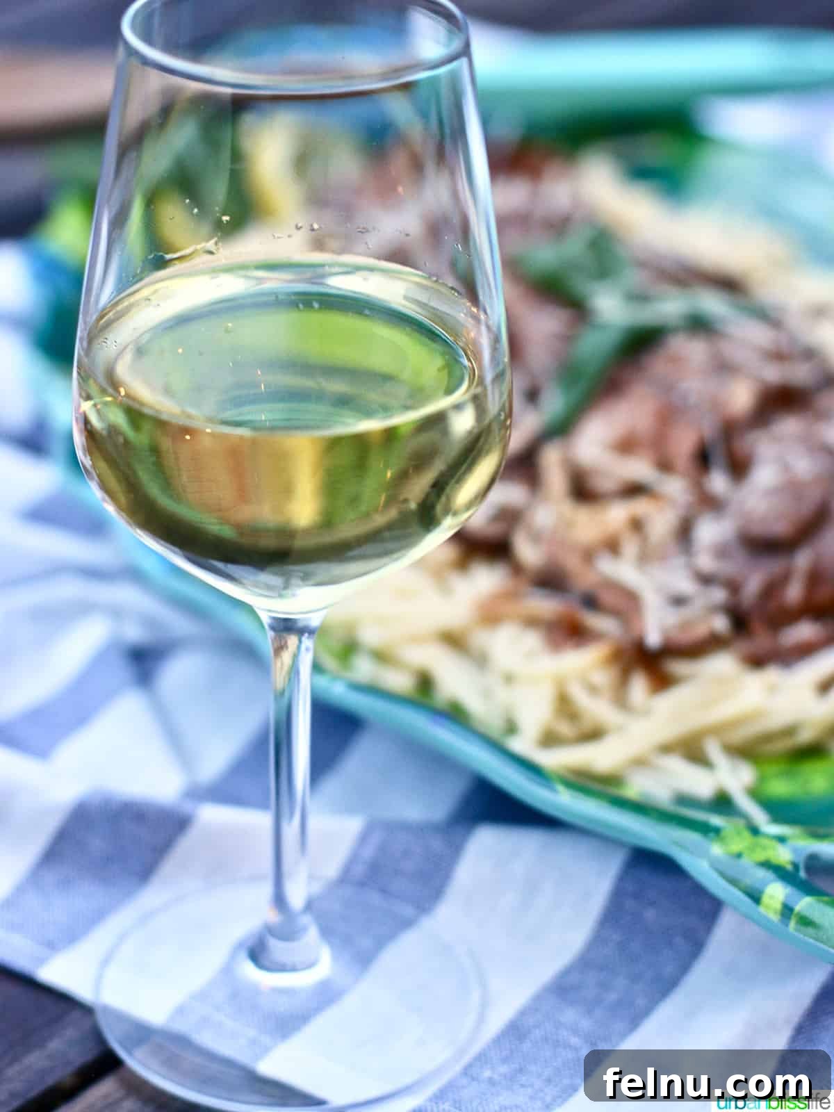 Perfect Wine Pairings for Every Chicken Dish 3 A glass of white wine set against a blurred background of a chicken marsala dish, highlighting the perfect pairing.