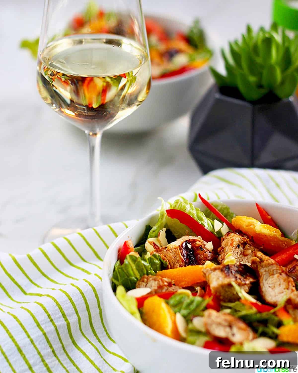 Perfect Wine Pairings for Every Chicken Dish 8 A bowl of mandarin orange chicken salad with almonds on a bed of greens, accompanied by a glass of white wine.