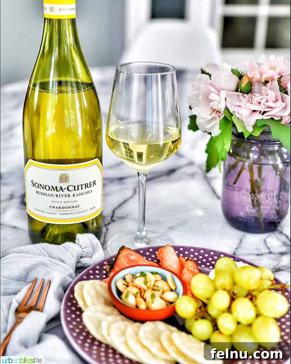 Chardonnay's Culinary Companions 5 A bottle and glass of Chardonnay white wine are presented with a plate of assorted snacks.