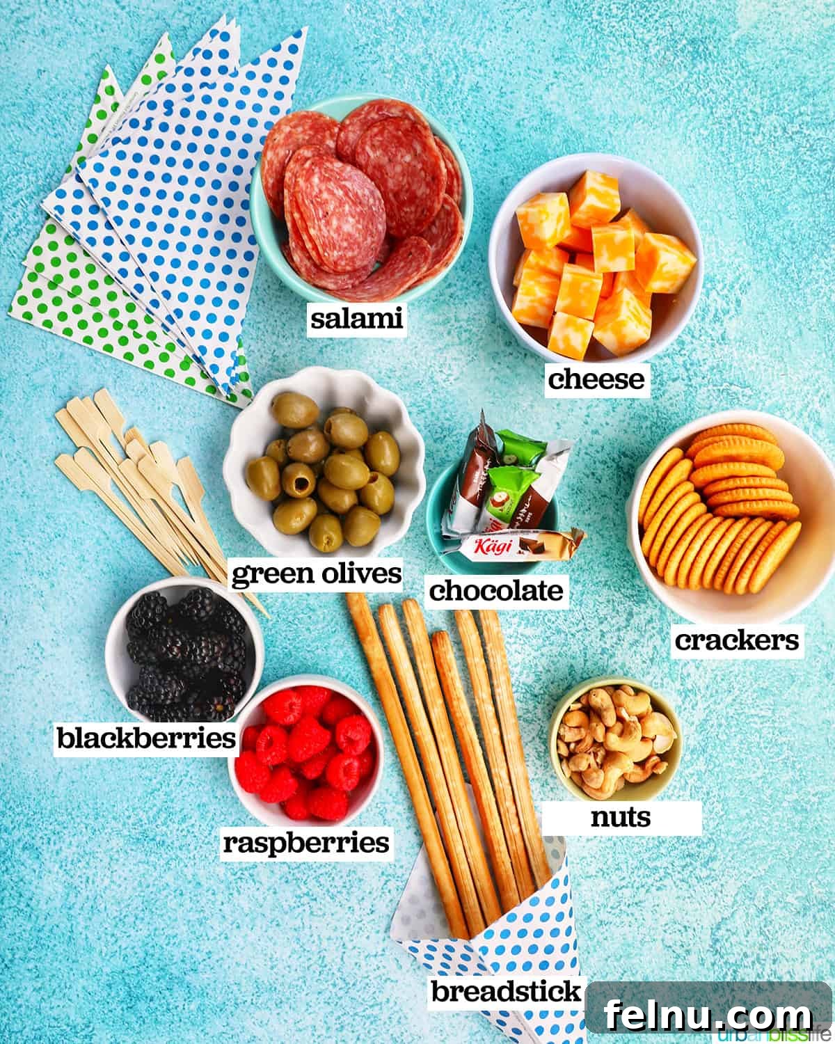 Charcuterie on the Go 5 Bowls of ingredients for making charcuterie cones, arranged on a blue background.