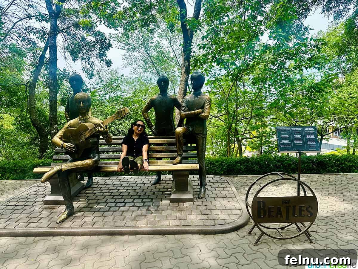 Explore Almaty: Thirty Unforgettable Things to Do 40 Marlynn Jayme Schotland sitting on the bench of The Beatles monument at Kok Tobe hill in Almaty, Kazakhstan, alongside life-sized statues of the band.