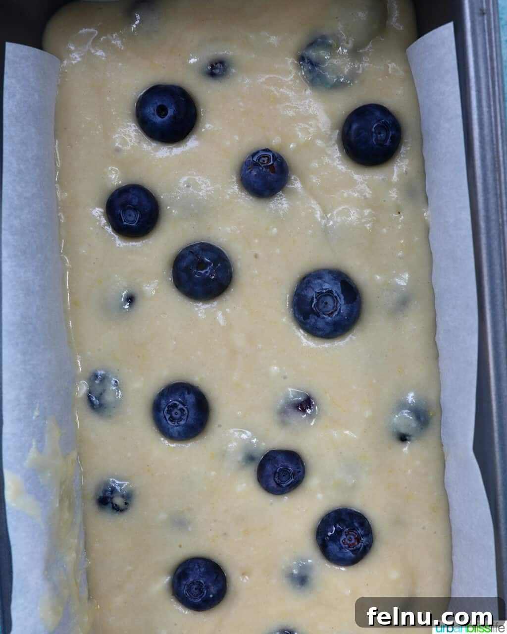 Lemon blueberry pound cake batter poured into a parchment paper-lined loaf pan, ready for baking.
