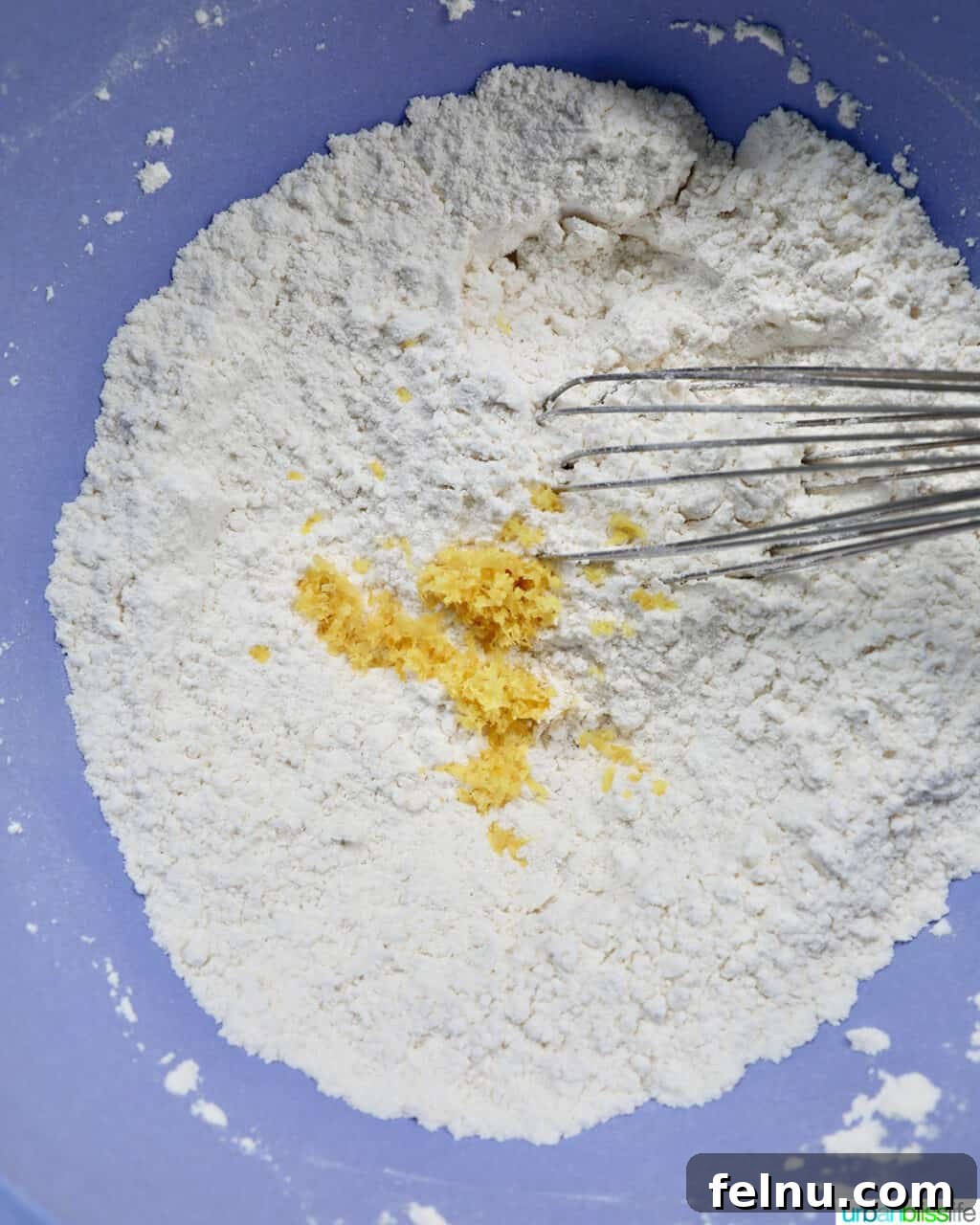 Dry ingredients, including flour and lemon zest, being whisked together in a bowl to ensure even distribution.