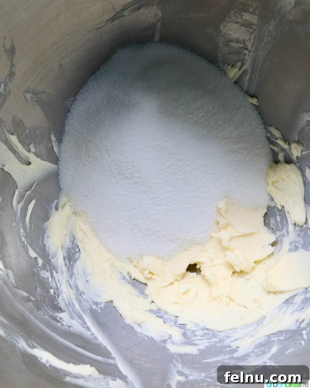 Sugar and butter being creamed together in a stainless steel mixing bowl.