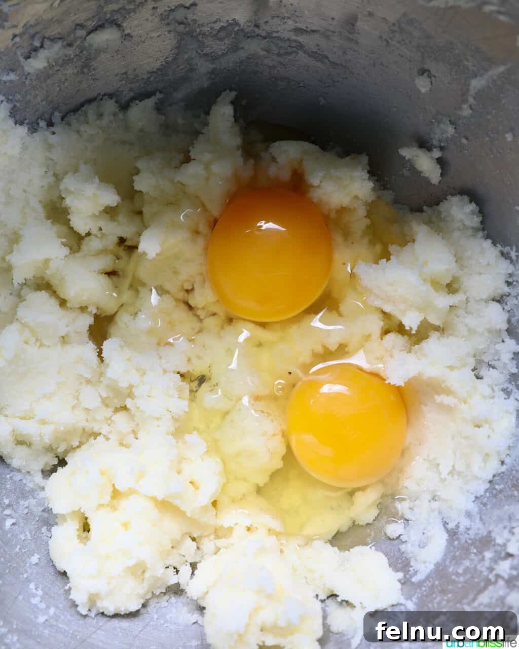 Eggs being added to the creamed butter and sugar mixture in a stainless steel bowl.