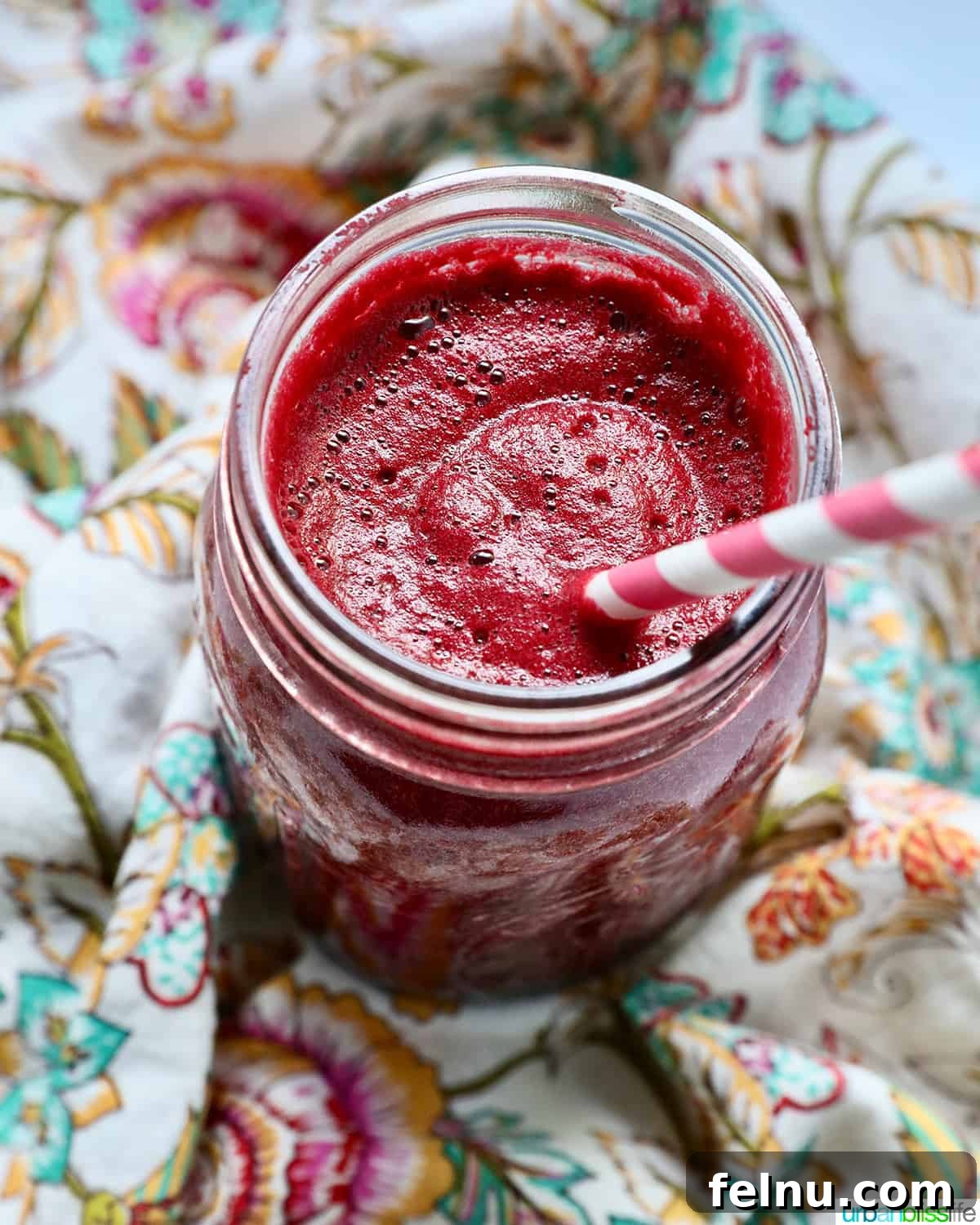 Ruby Root Revival 2 mason jar with red beet juice, a pink and white straw, on a colorful napkin.
