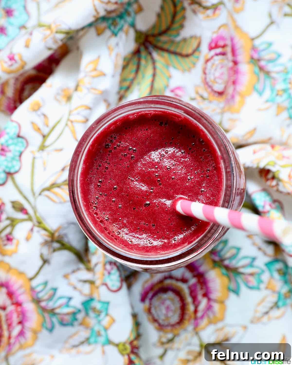 Ruby Root Revival 3 mason jar with red beet juice, a pink and white straw, on a colorful napkin.