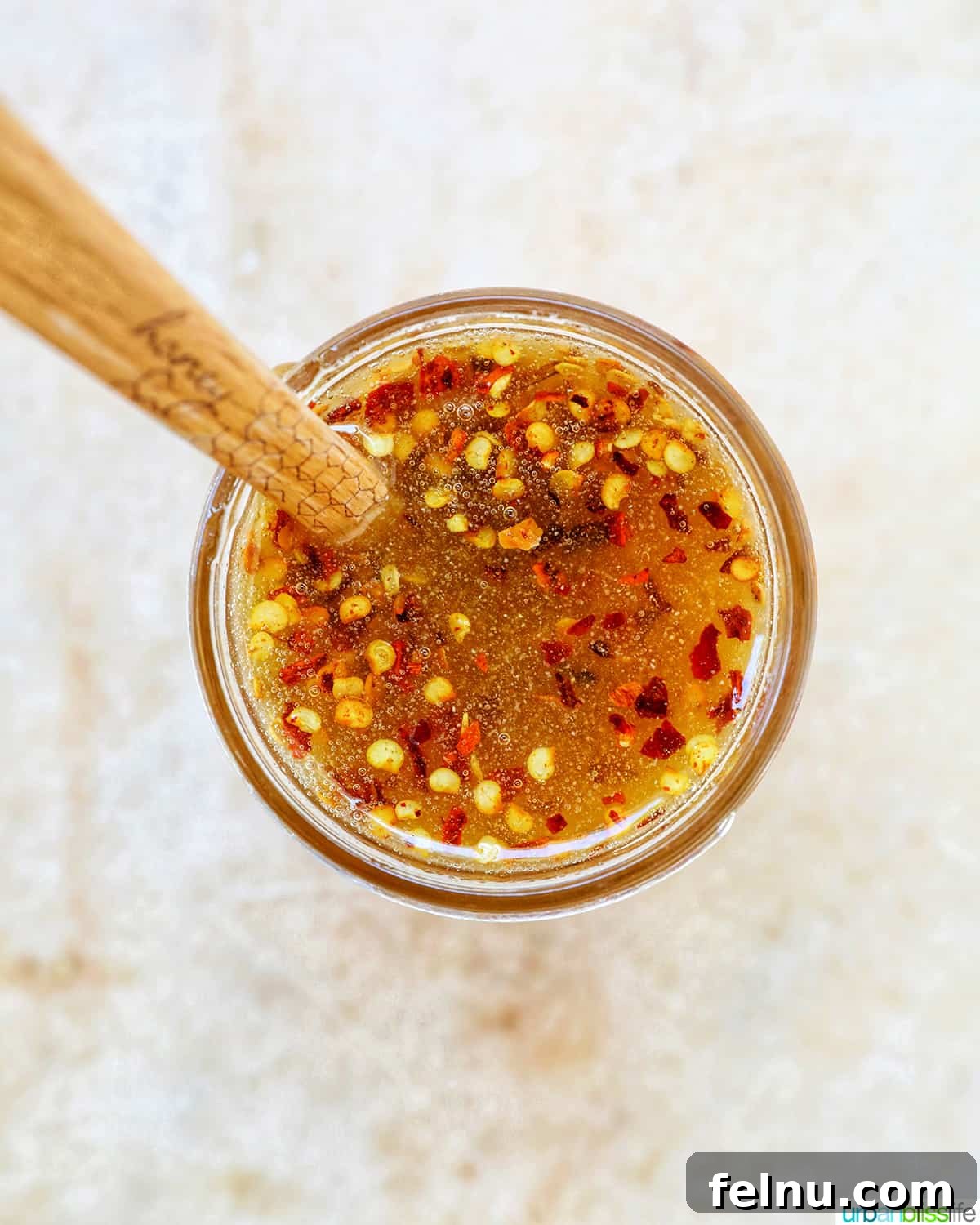 Overhead shot of a wooden spoon emerging from a jar of homemade Hot Honey Sauce.