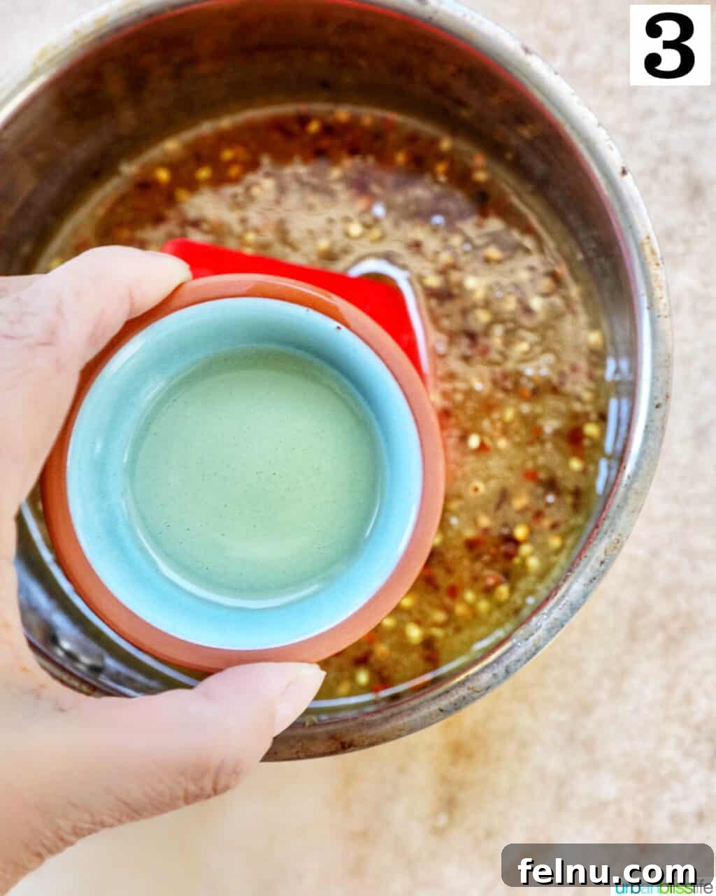 Hand pouring apple cider vinegar into the Hot Honey Sauce mixture in a saucepan.