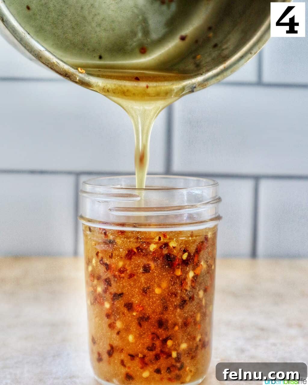 Pouring freshly made Hot Honey Sauce from a saucepan into a clean mason jar.