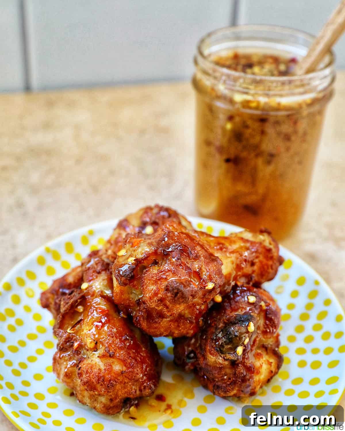 Jar of Hot Honey Sauce behind a plate of perfectly glazed Hot Honey Chicken Wings.