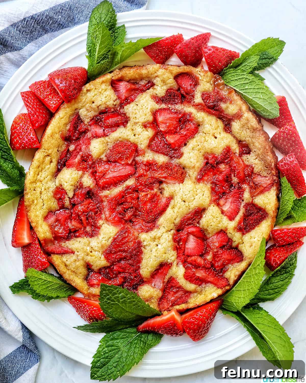 Overhead view of Strawberry Spoon Cake garnished with mint leaves and sliced strawberries on a white plate.