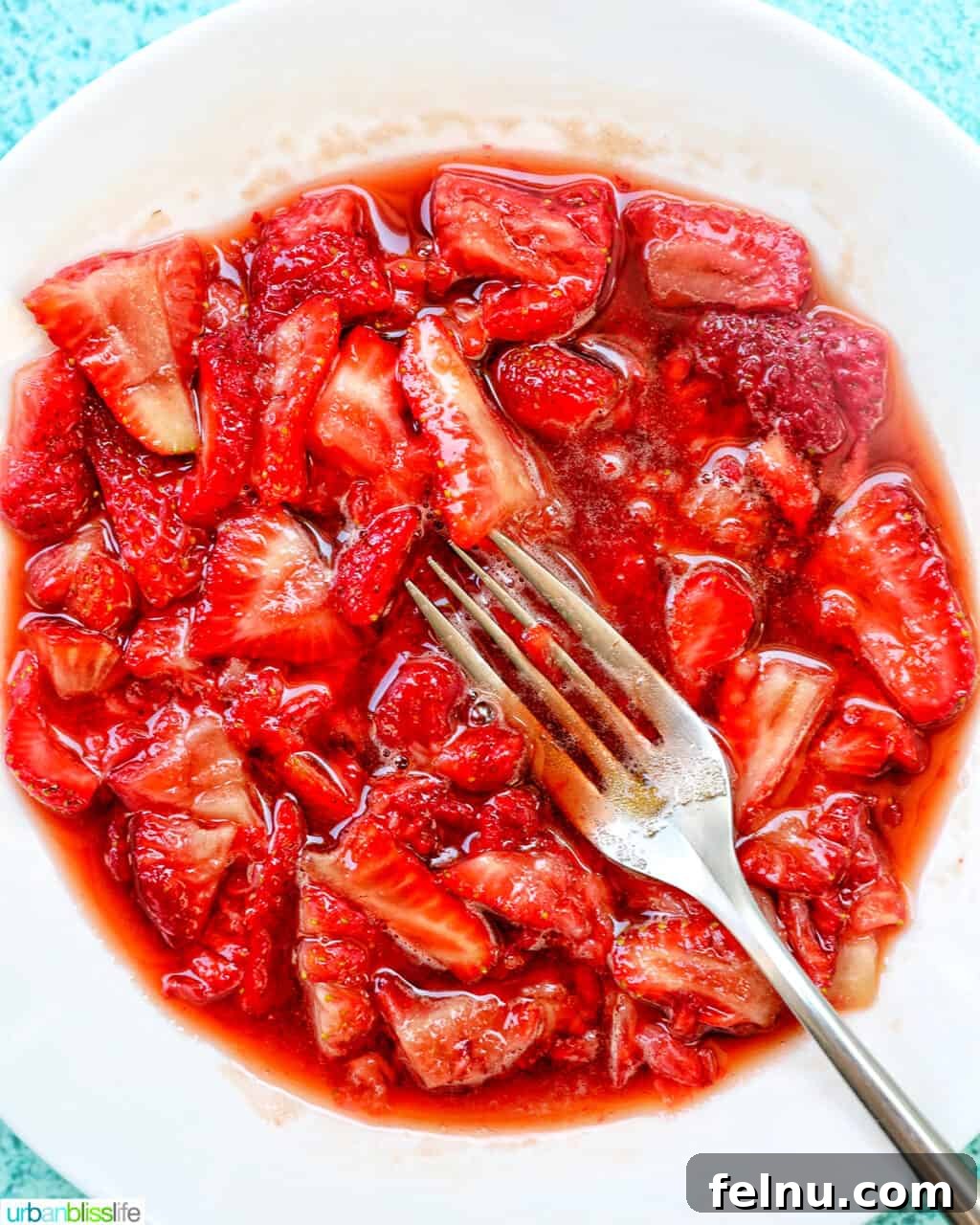Fork mashing strawberries in a white bowl.