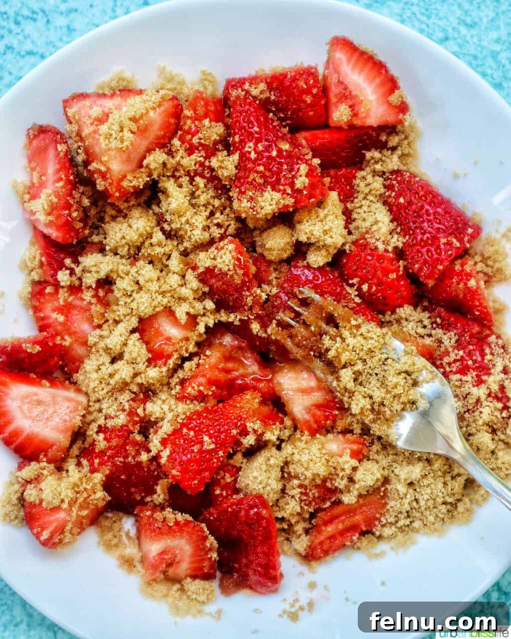 Fork mashing fresh strawberries and brown sugar together.