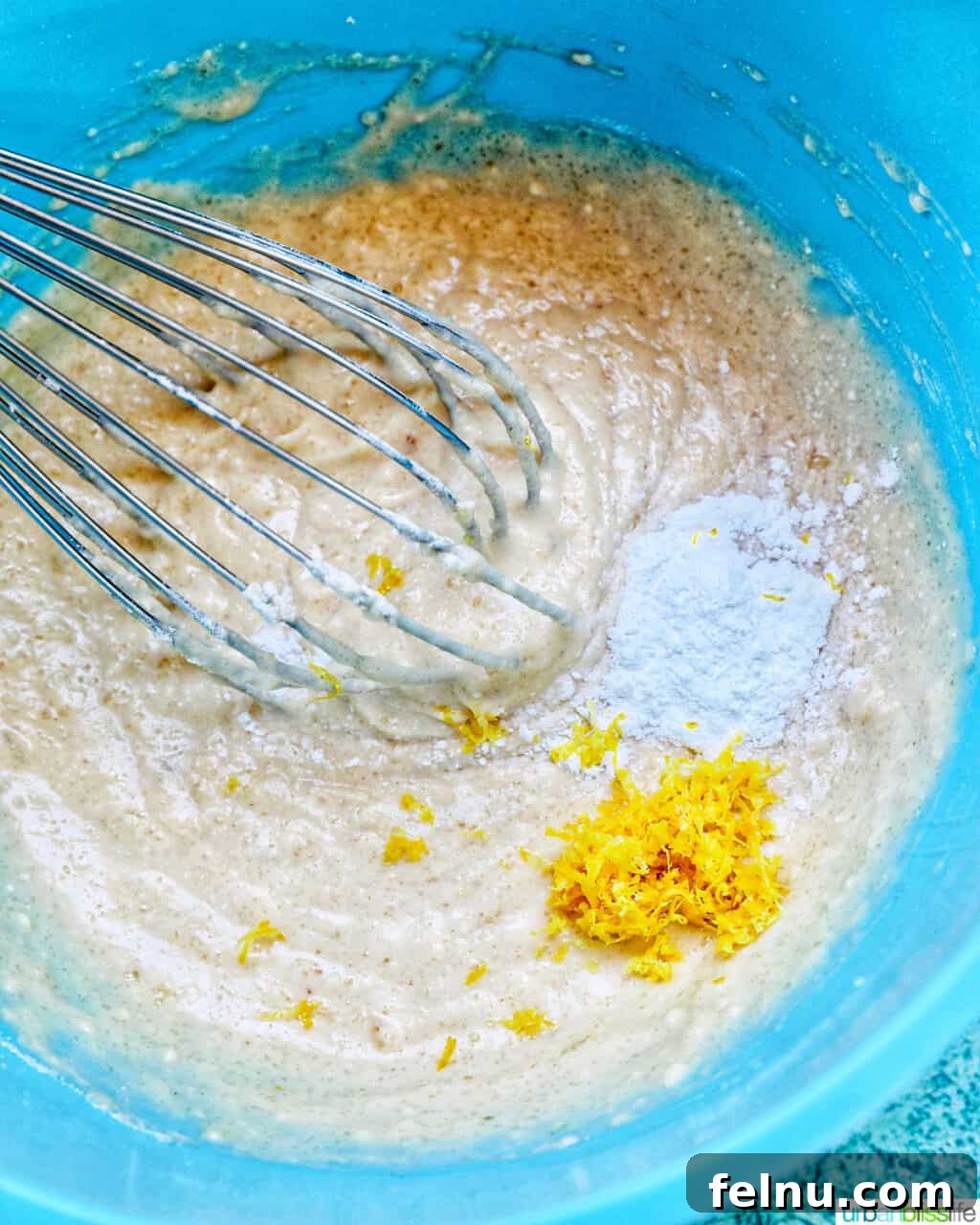 Whisk in cake batter with lemon zest in a blue bowl.