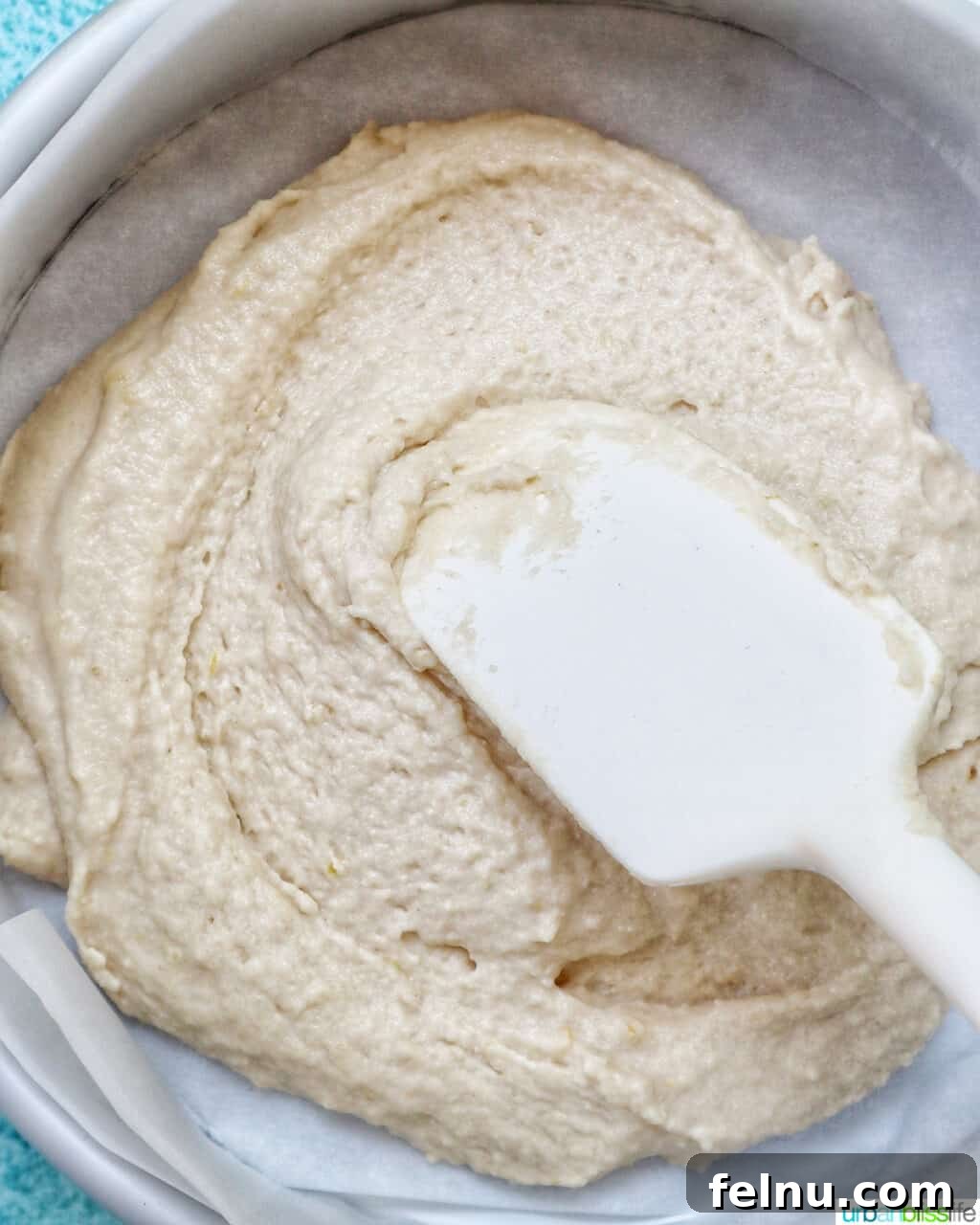 White spatula smoothing out Strawberry Spoon Cake batter in a parchment paper-lined baking pan.