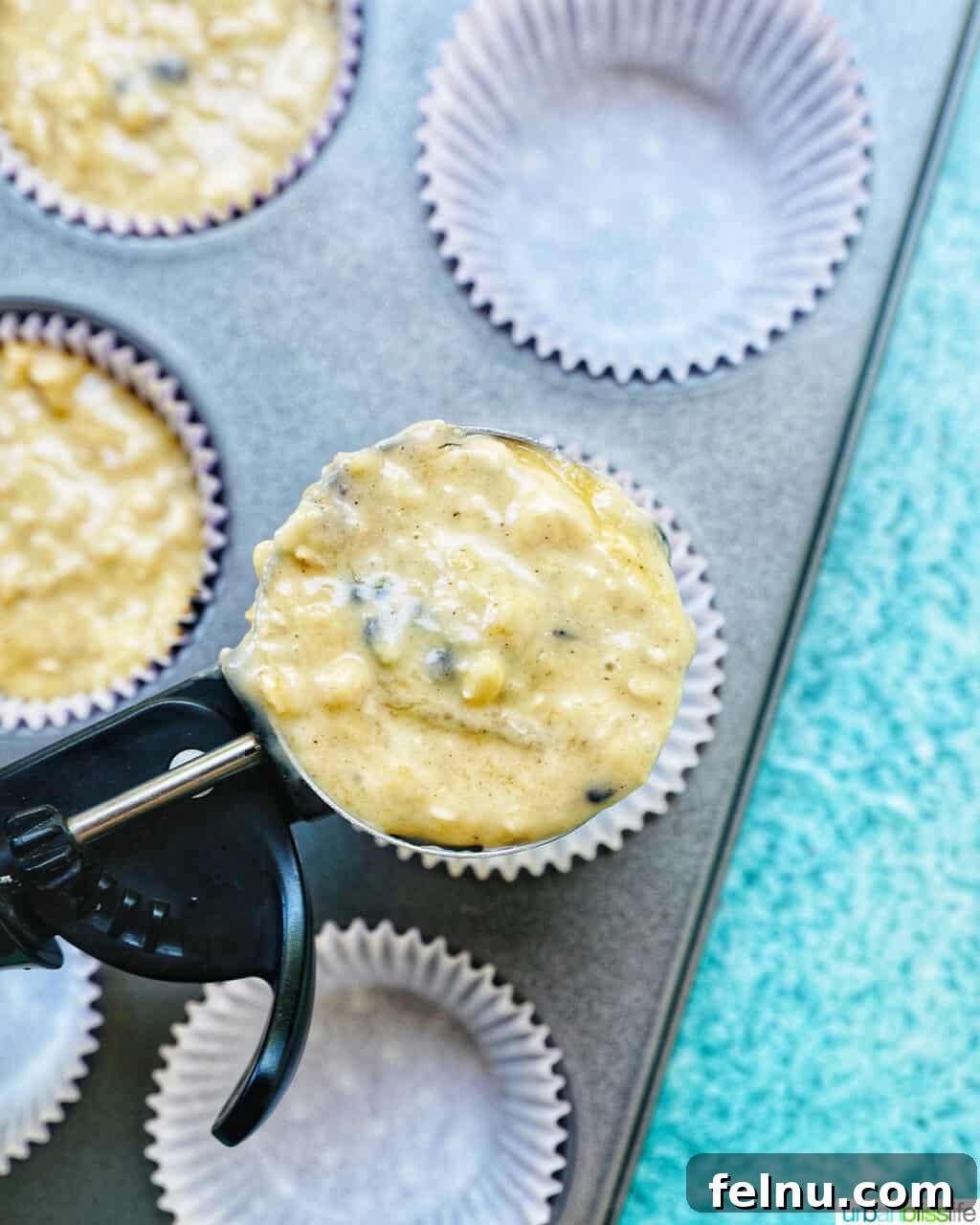 Bursting Blackberry Banana Oat Muffins 13 A scoop of muffin batter is shown suspended over prepared muffin cups lined with paper, ready to be filled.
