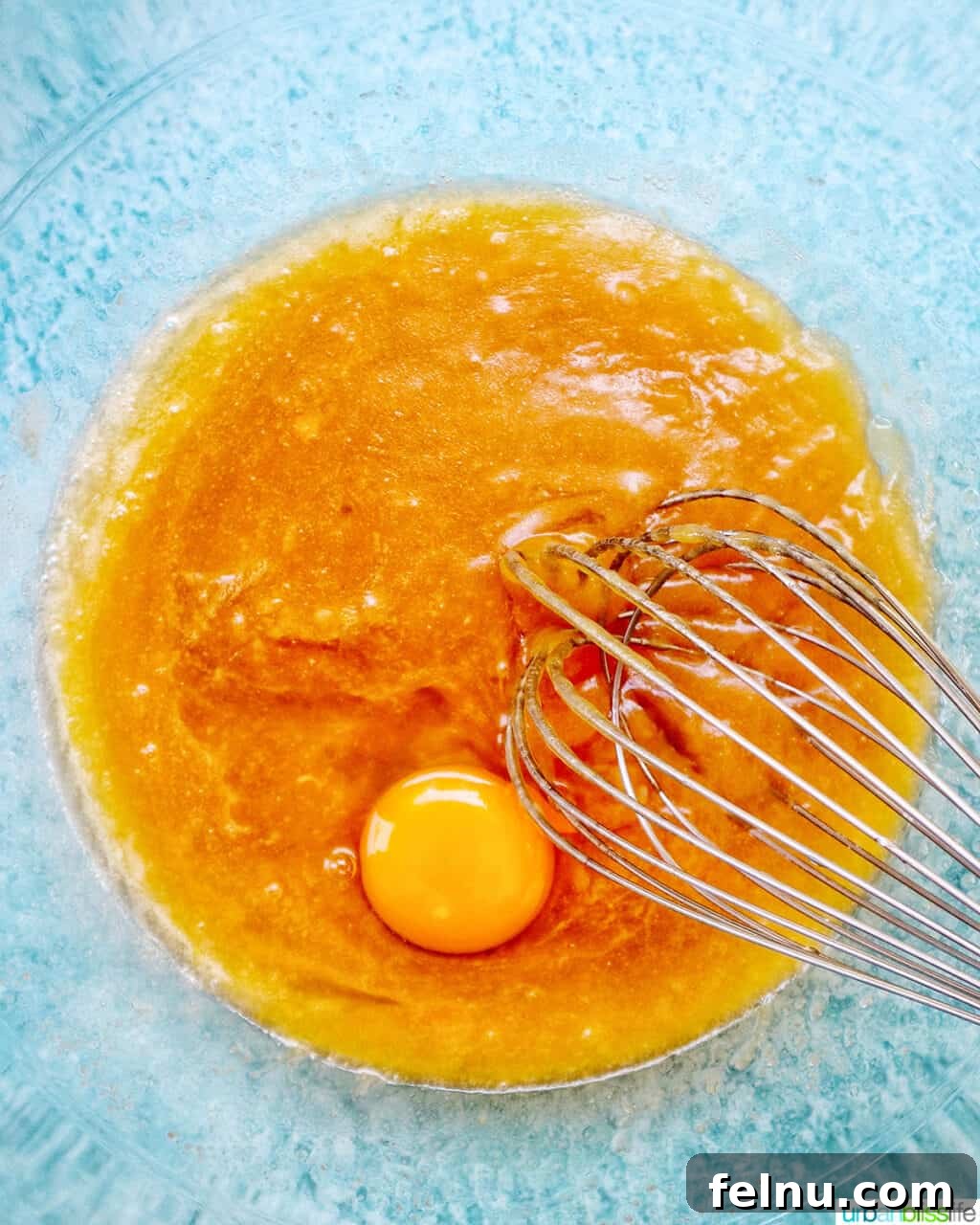 Bursting Blackberry Banana Oat Muffins 8 A whisk is shown mixing wet ingredients in a clear bowl, with an egg yolk visible among them, indicating the eggs are being incorporated.