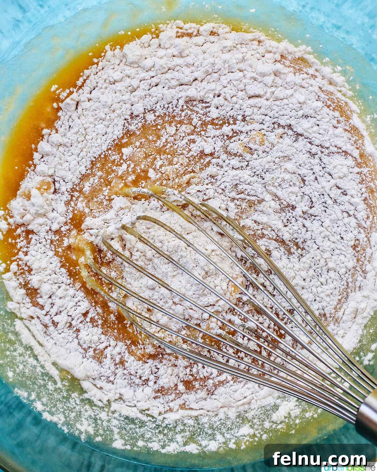 Bursting Blackberry Banana Oat Muffins 10 Dry ingredients are being whisked into wet ingredients in a clear mixing bowl, showing the merging of the two mixtures.