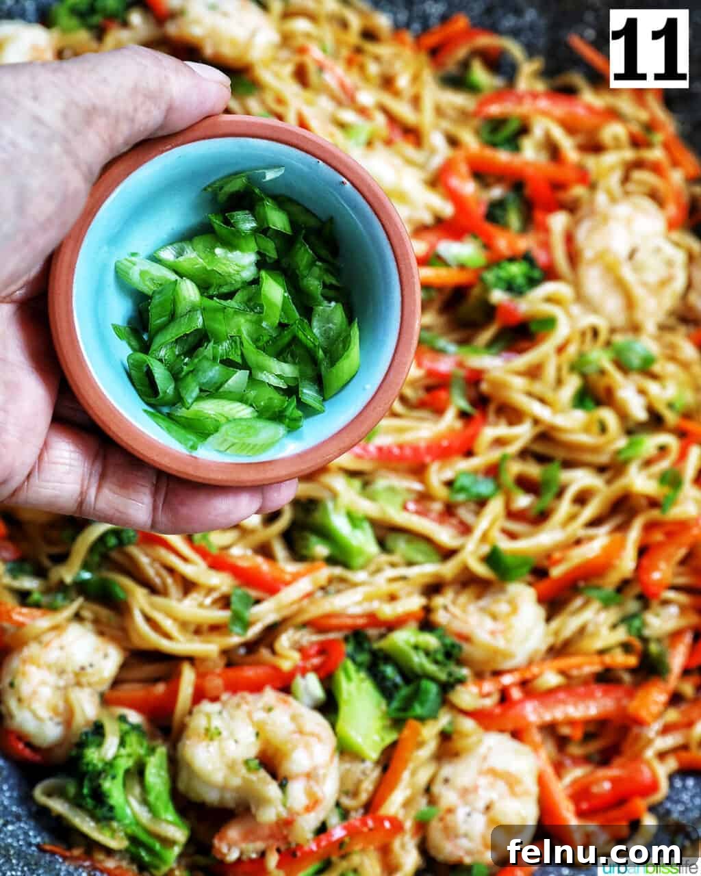Homemade Prawn Chow Mein Delight 18 A hand garnishing a wok full of Prawn Chow Mein with freshly chopped green onions.