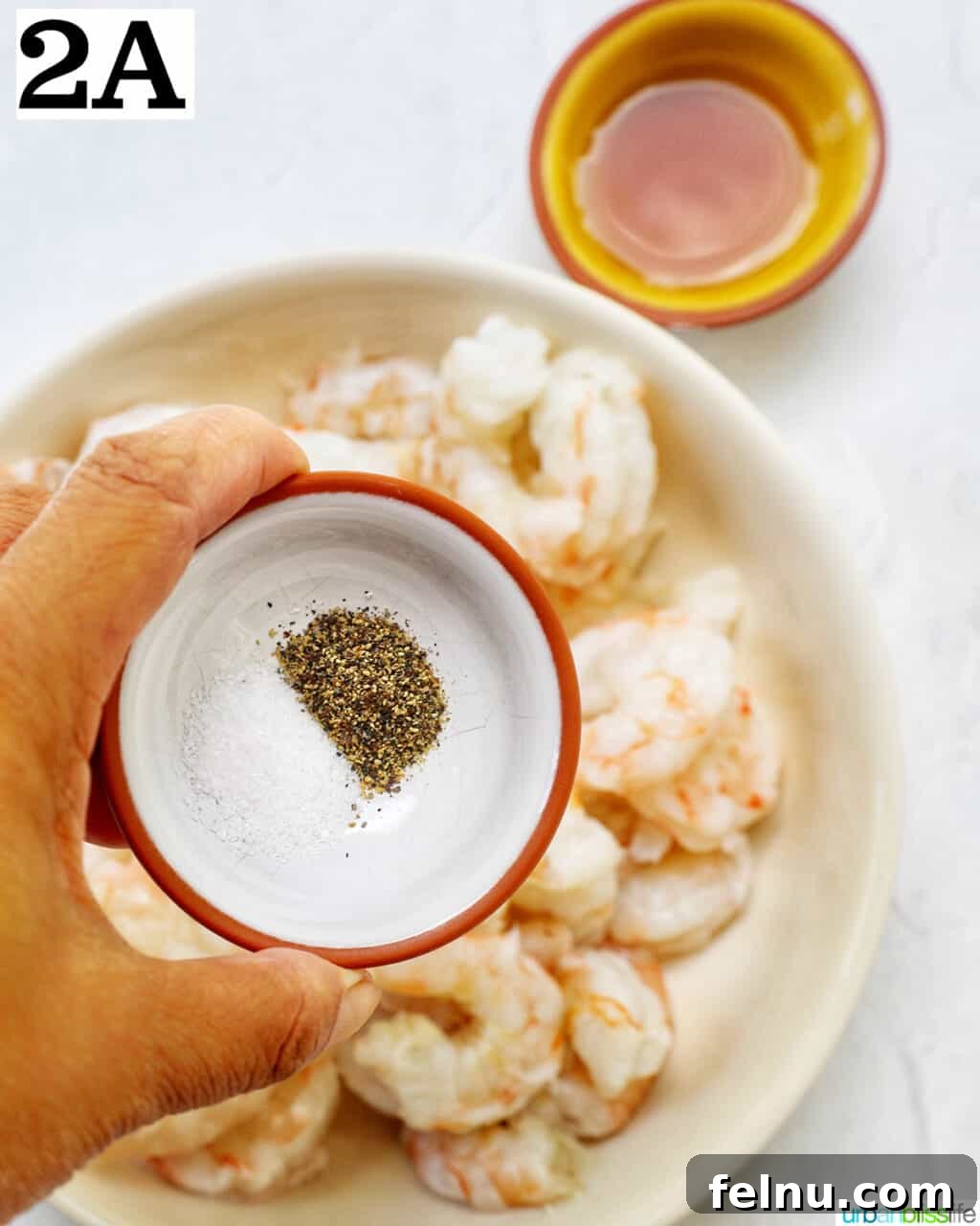 Homemade Prawn Chow Mein Delight 7 A hand seasoning prawns with salt and pepper in a bowl, preparing them for cooking.