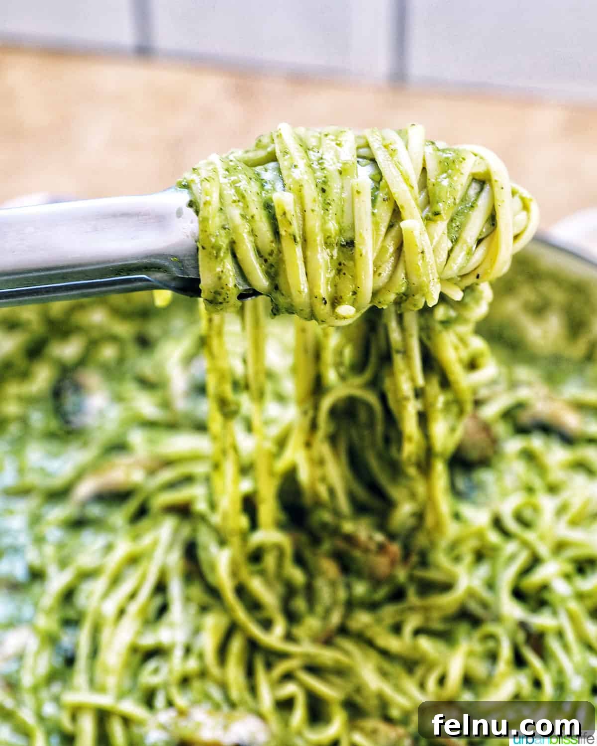 Earthy Mushroom Pesto Pasta 17 Kitchen tongs twirling linguine pasta coated in creamy mushroom pesto sauce in a serving bowl.