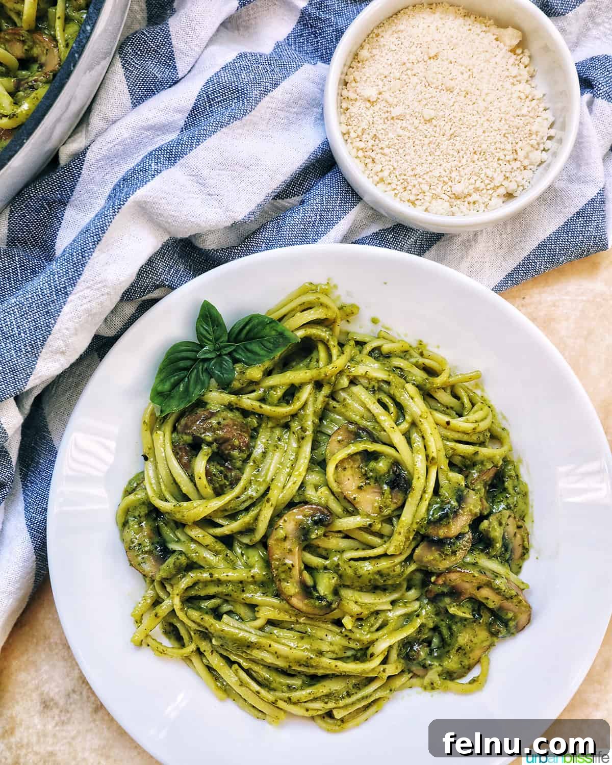 Earthy Mushroom Pesto Pasta 18 Bowl of creamy mushroom pesto pasta, ready to be served, with a side of grated parmesan cheese.