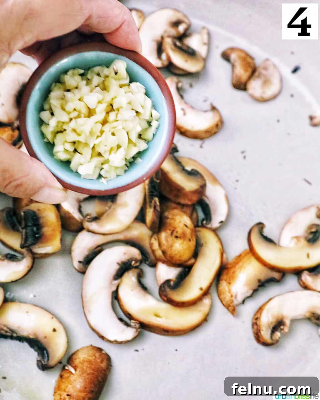 Earthy Mushroom Pesto Pasta 8 Hand holding a small bowl of minced garlic over chopped mushrooms cooking in a pan.