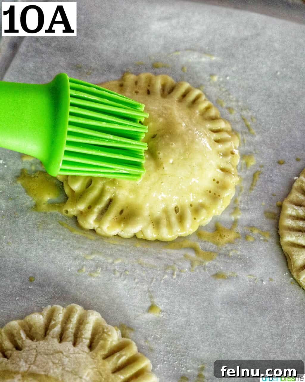 Sun-Kissed Peach Mango Pie 14 A green pastry brush applying egg wash onto a mini peach mango hand pie.