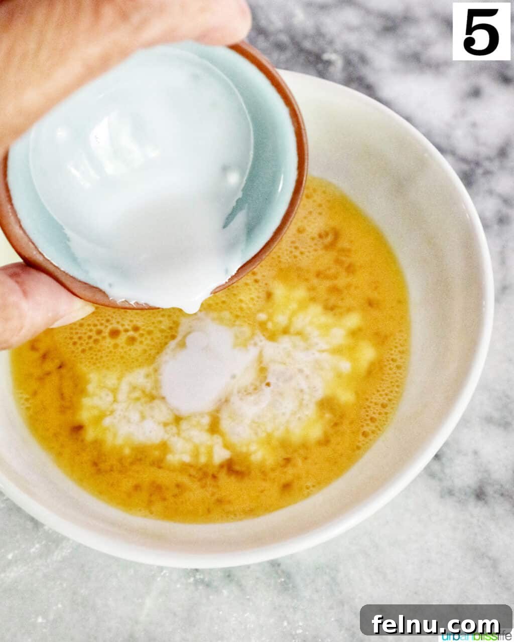 Sun-Kissed Peach Mango Pie 9 Hand pouring cream into a bowl of beaten eggs to create an egg wash.