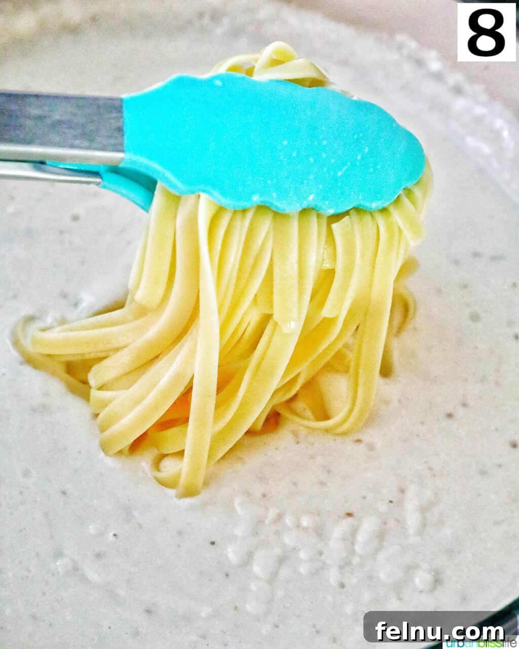 Velvety Salmon Pasta 15 Blue tongs carefully transferring cooked pasta directly into the creamy sauce in a large skillet.