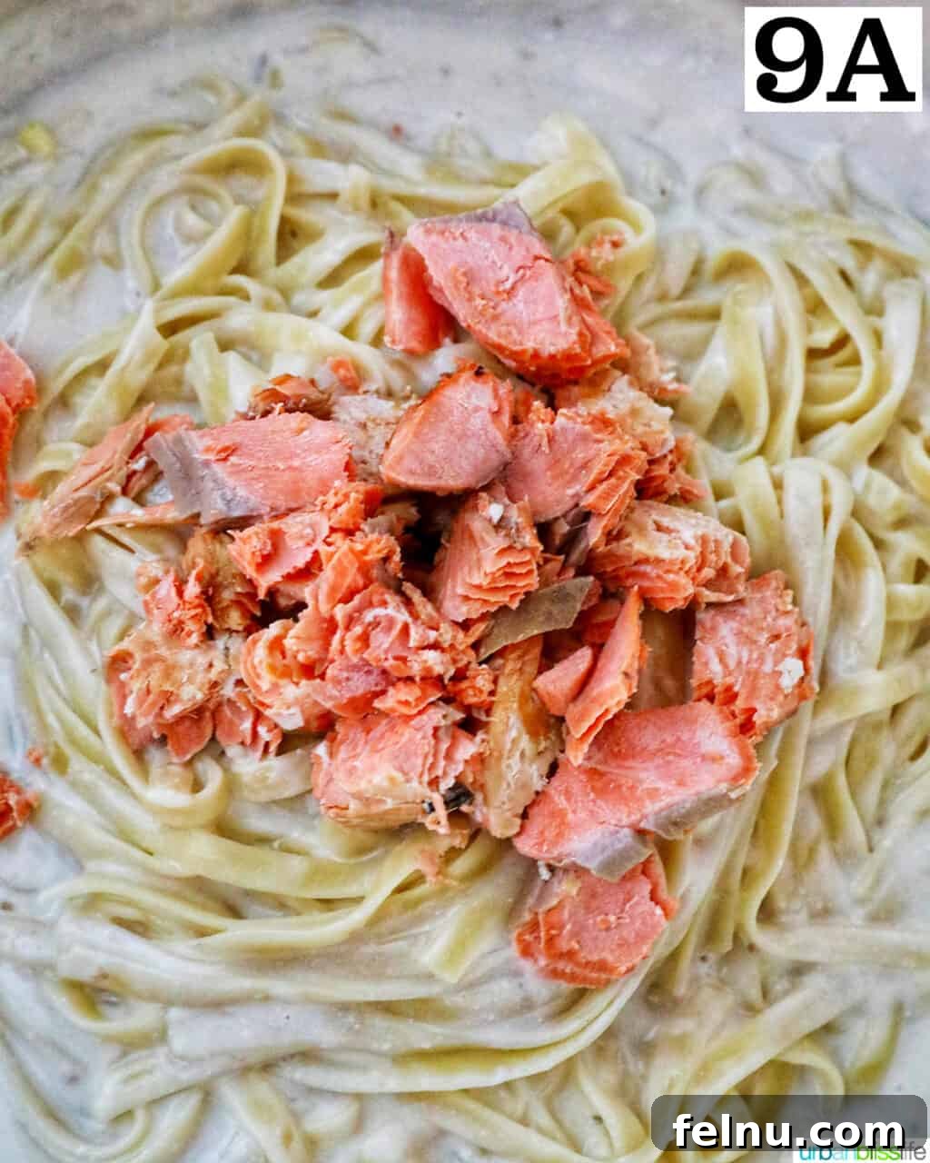 Velvety Salmon Pasta 16 Flaked salmon chunks being added to the pasta and cream sauce mixture in a skillet, ready to be combined.