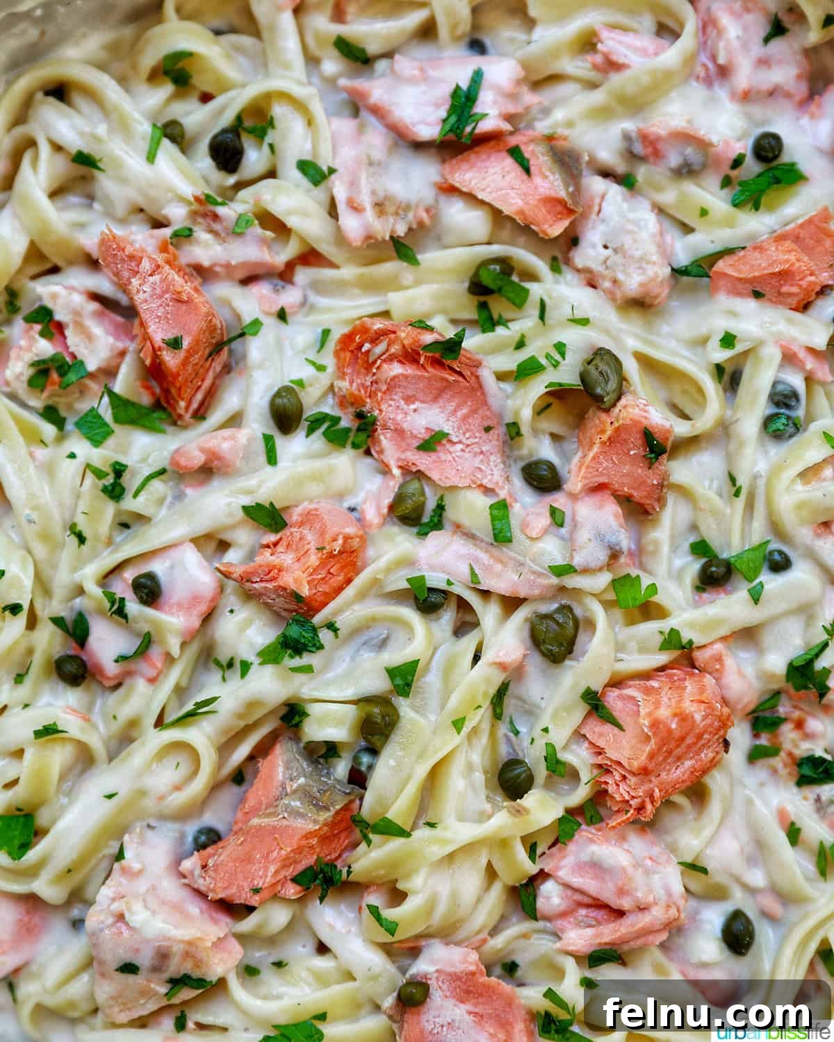 Velvety Salmon Pasta 18 A close-up view of Pasta Alla Salmone in a large saucepan, showcasing the creamy texture and flakes of salmon, with parsley and lemon garnishes.