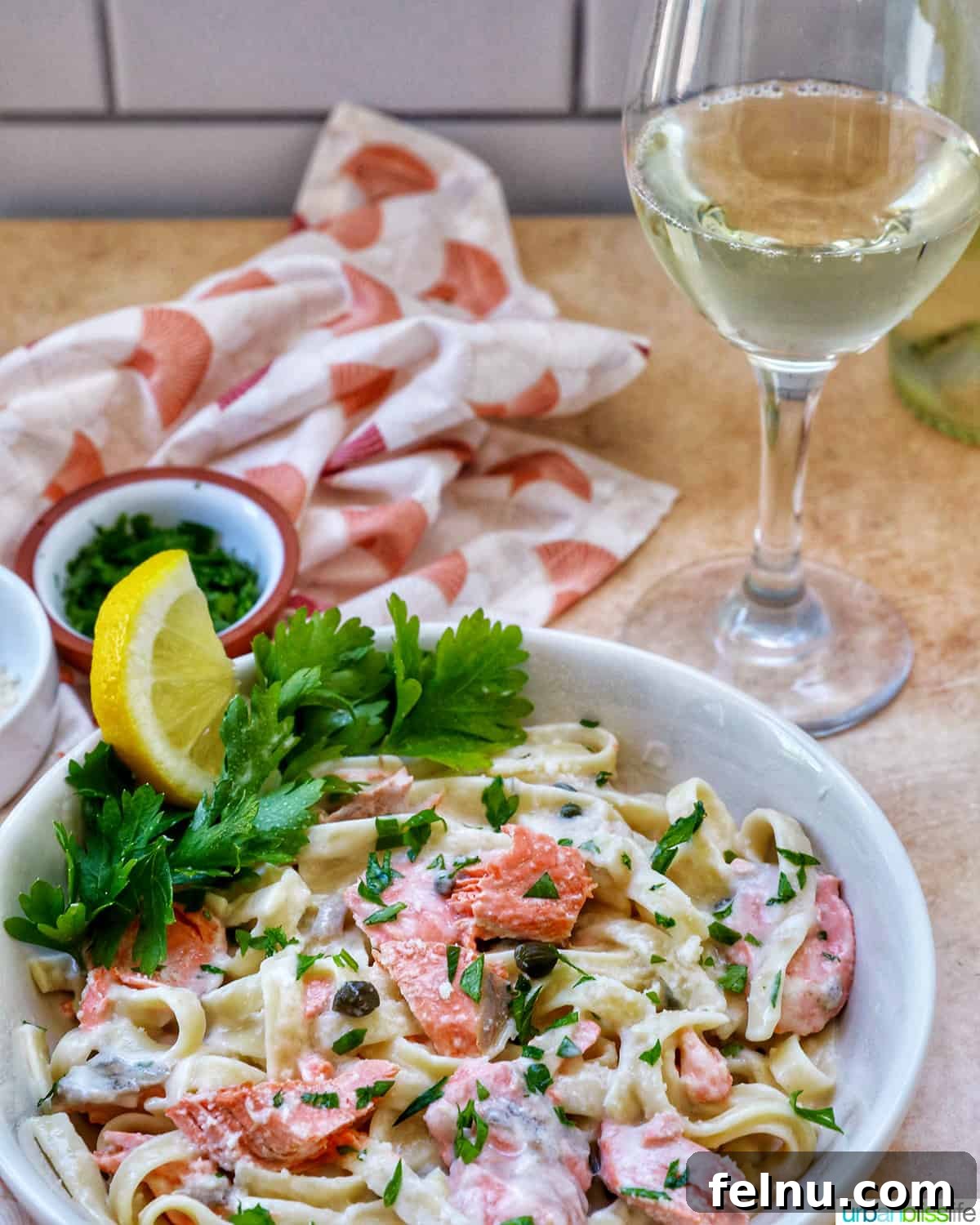 Velvety Salmon Pasta 20 A white bowl of creamy pasta alla salmone, garnished with parsley and lemon, positioned next to a clear glass of white wine.
