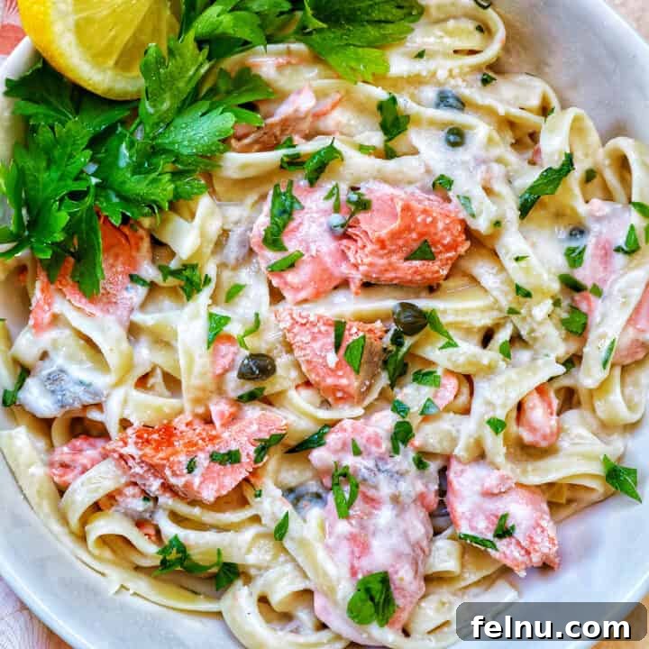 A serving of Pasta Alla Salmone in a white bowl, garnished with fresh parsley and lemon slices.