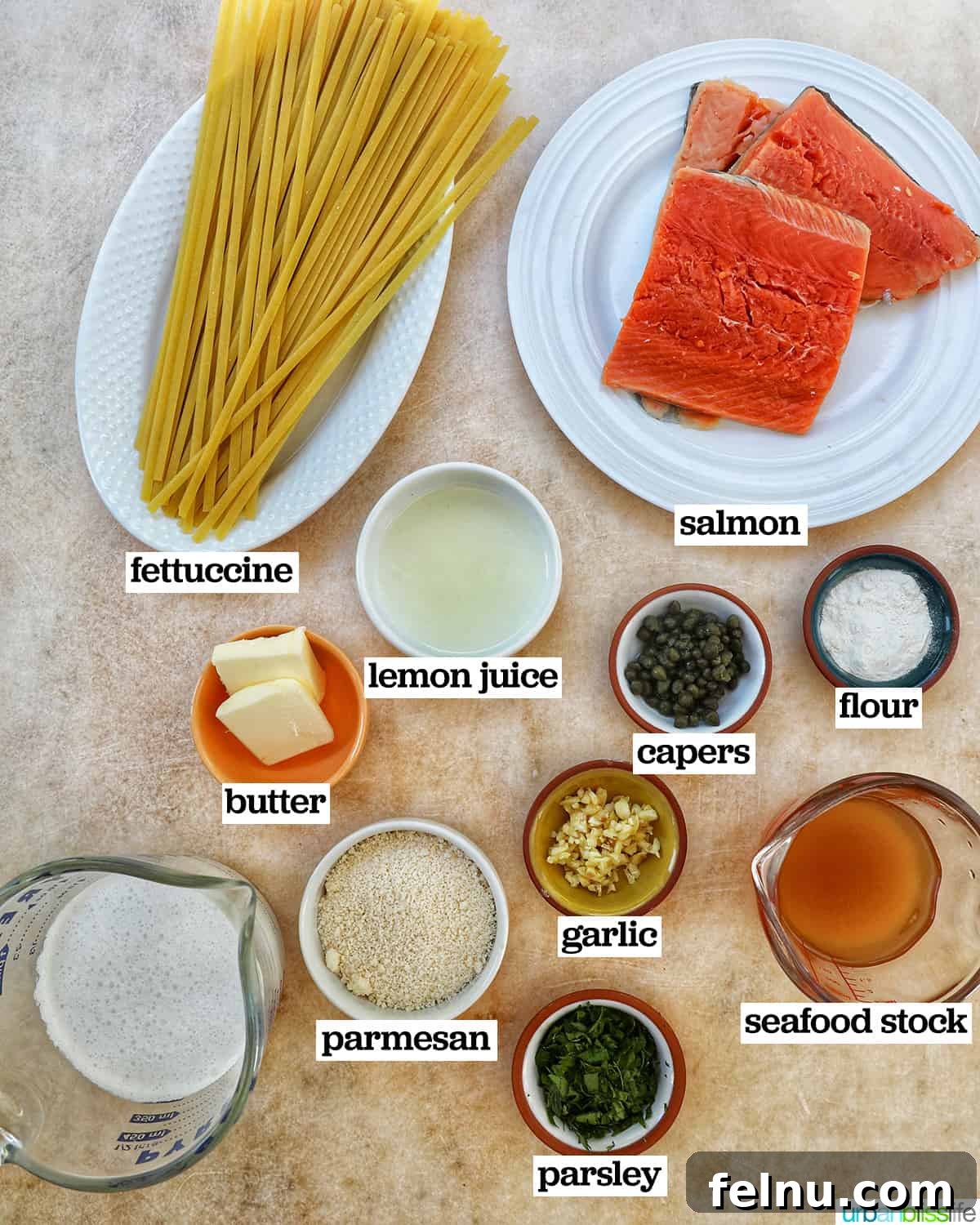 Velvety Salmon Pasta 4 Separate bowls displaying fresh ingredients for salmon pasta, including salmon fillets, pasta, fresh herbs, lemon, and capers.