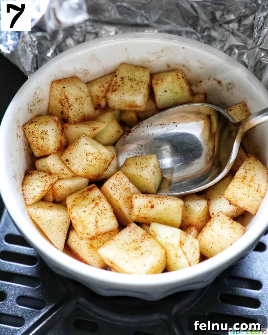 Air Fryer Apple Crumble 13 White bowl with spiced apples and a spoon in an air fryer basket.