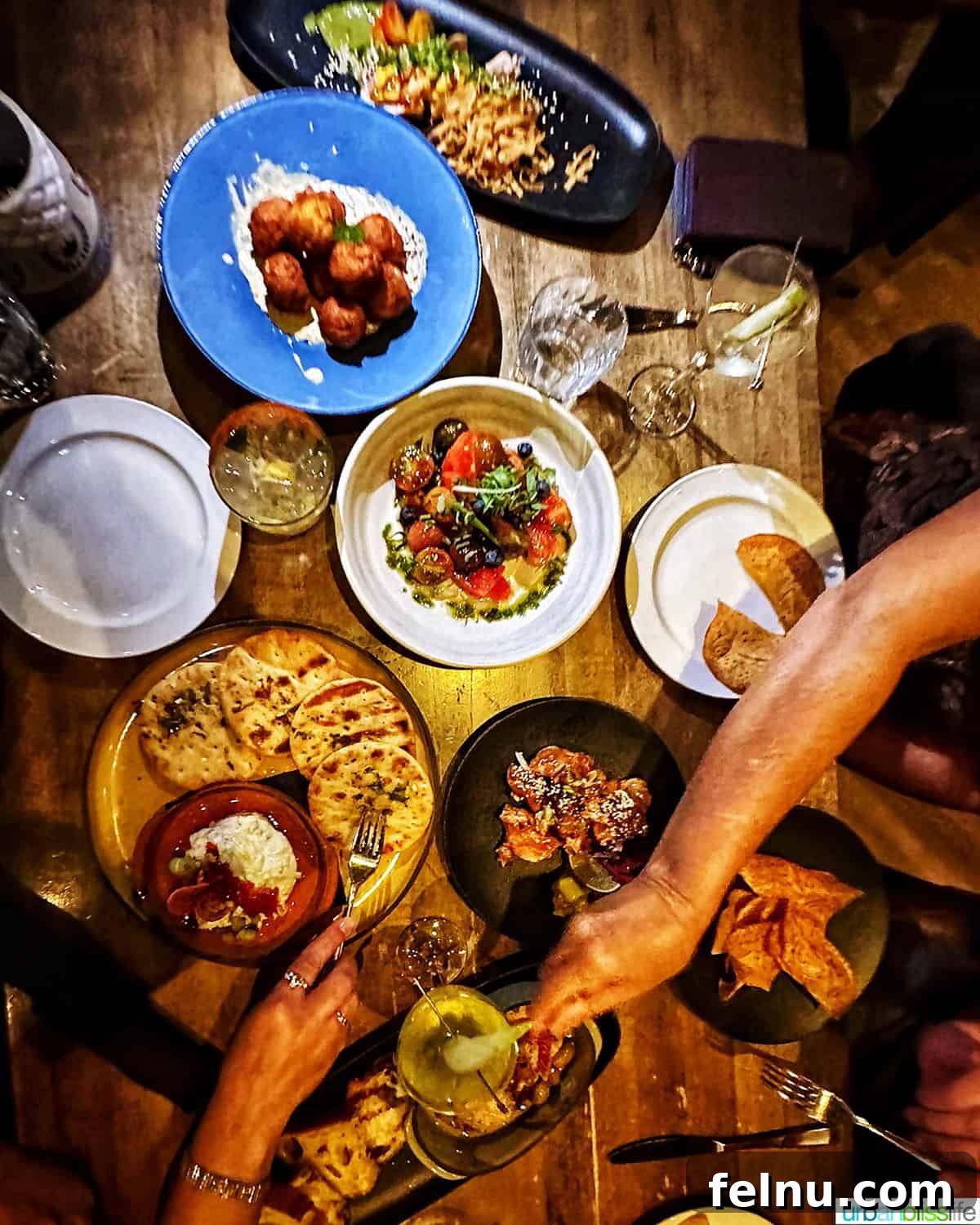 Whistler Village Signature Escape 10 Overhead shot of a rustic wooden table laden with various gourmet dishes and cocktails at The Raven Room, a popular restaurant in Whistler, British Columbia, with hands reaching for food.