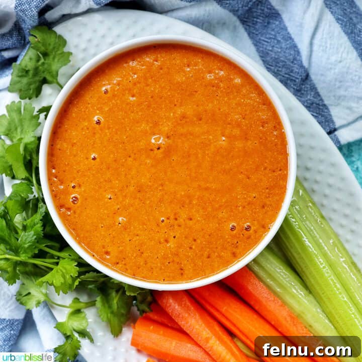 bowl of vegan buffalo sauce on a plate with carrot and celery sticks and parsley garnish.