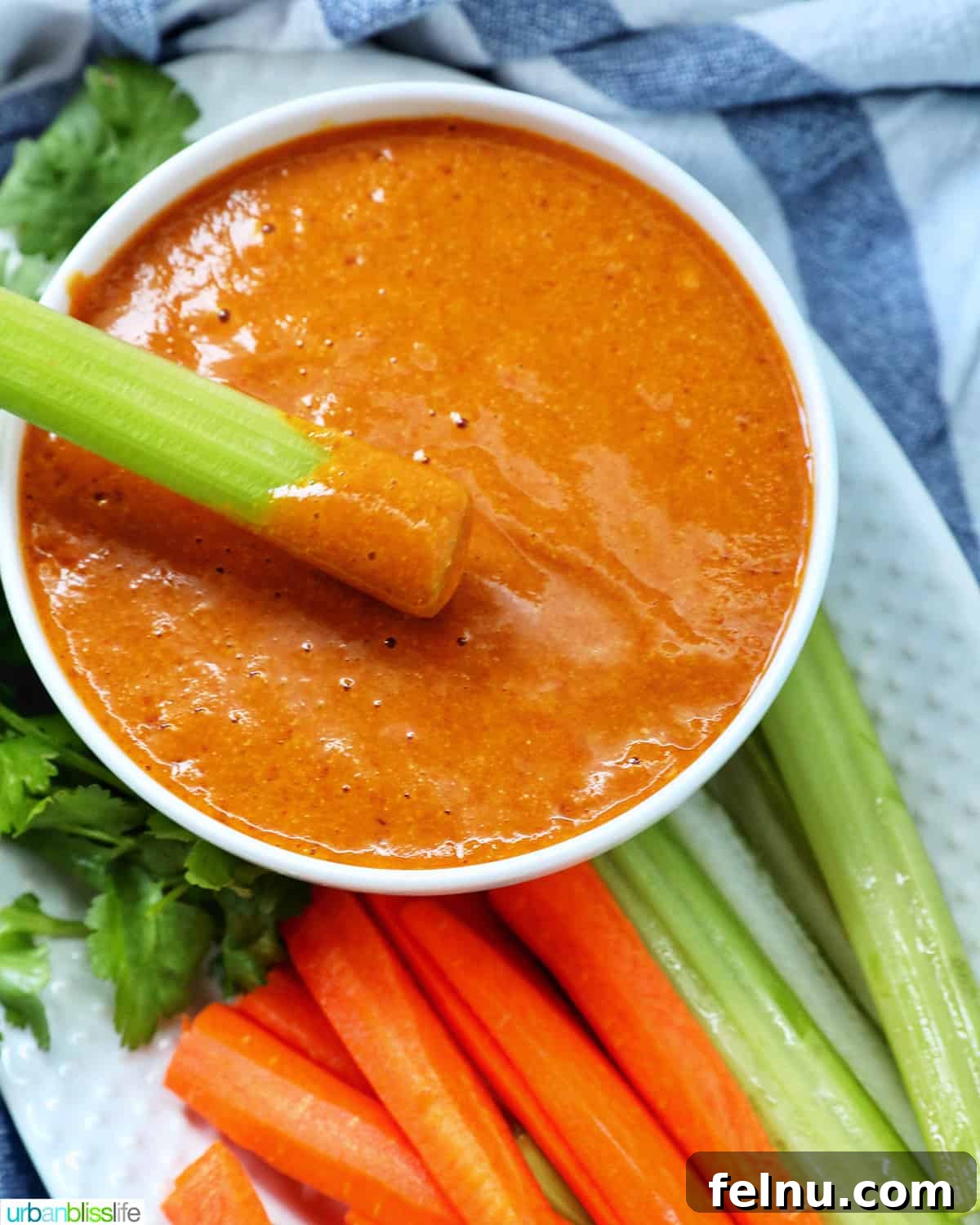 Carrot stick dipped in vegan buffalo sauce